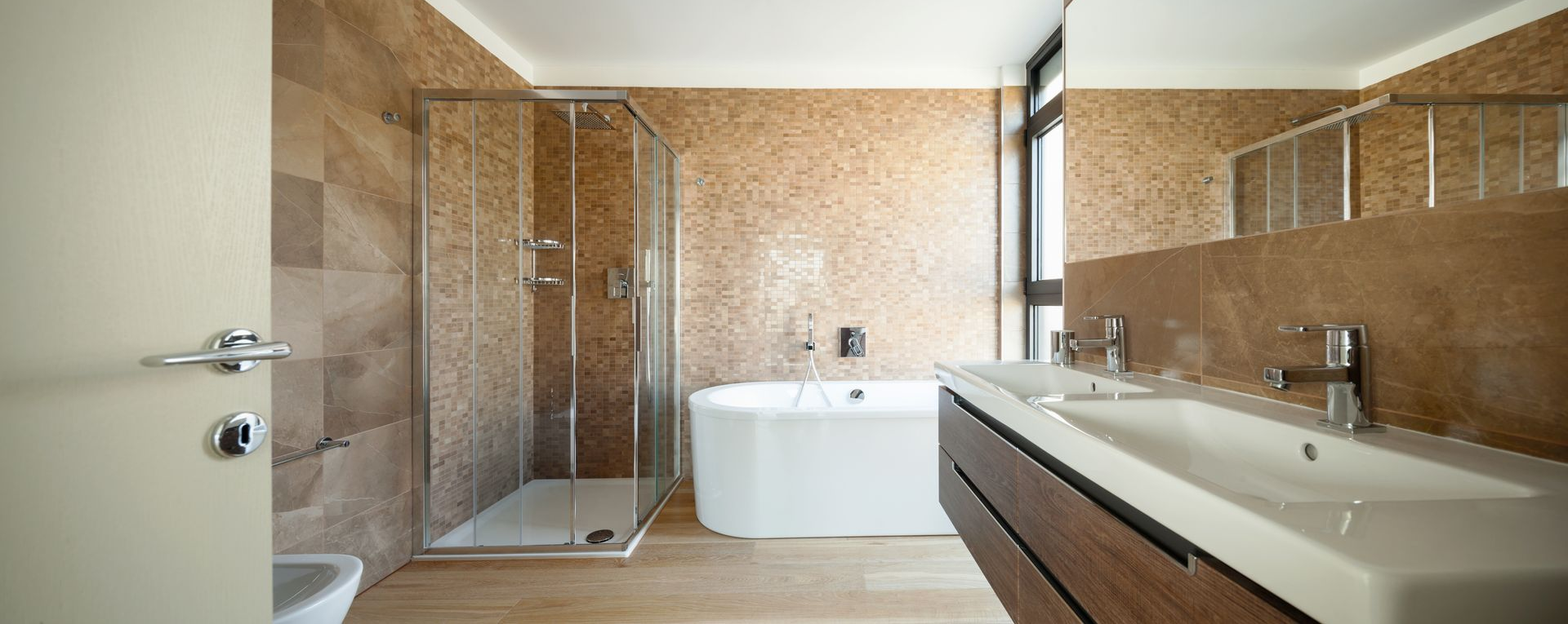 Salle de bains moderne avec douche en verre, baignoire, double vasque et murs carrelés.