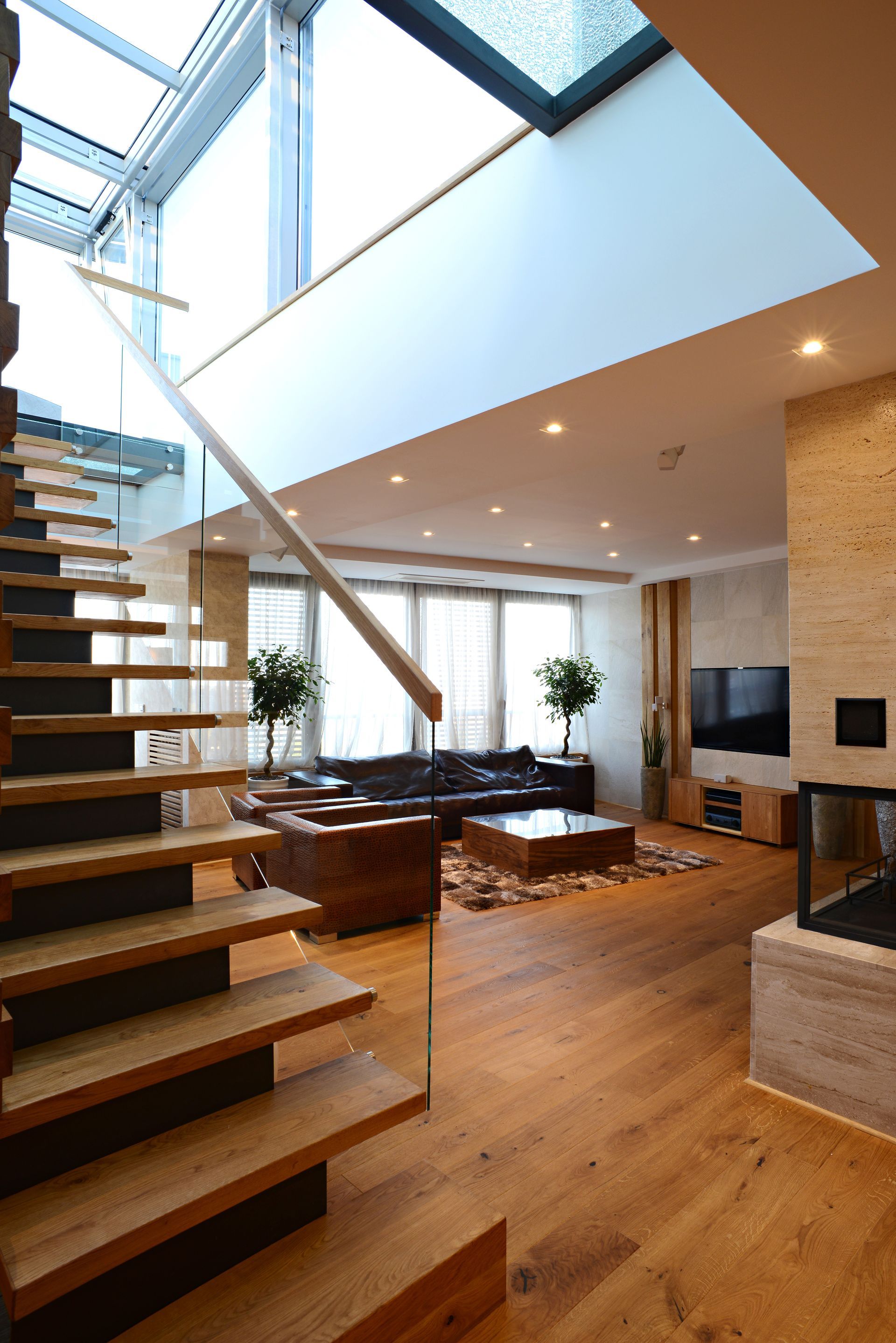 Salon moderne avec escalier en bois, meubles en cuir et puits de lumière.