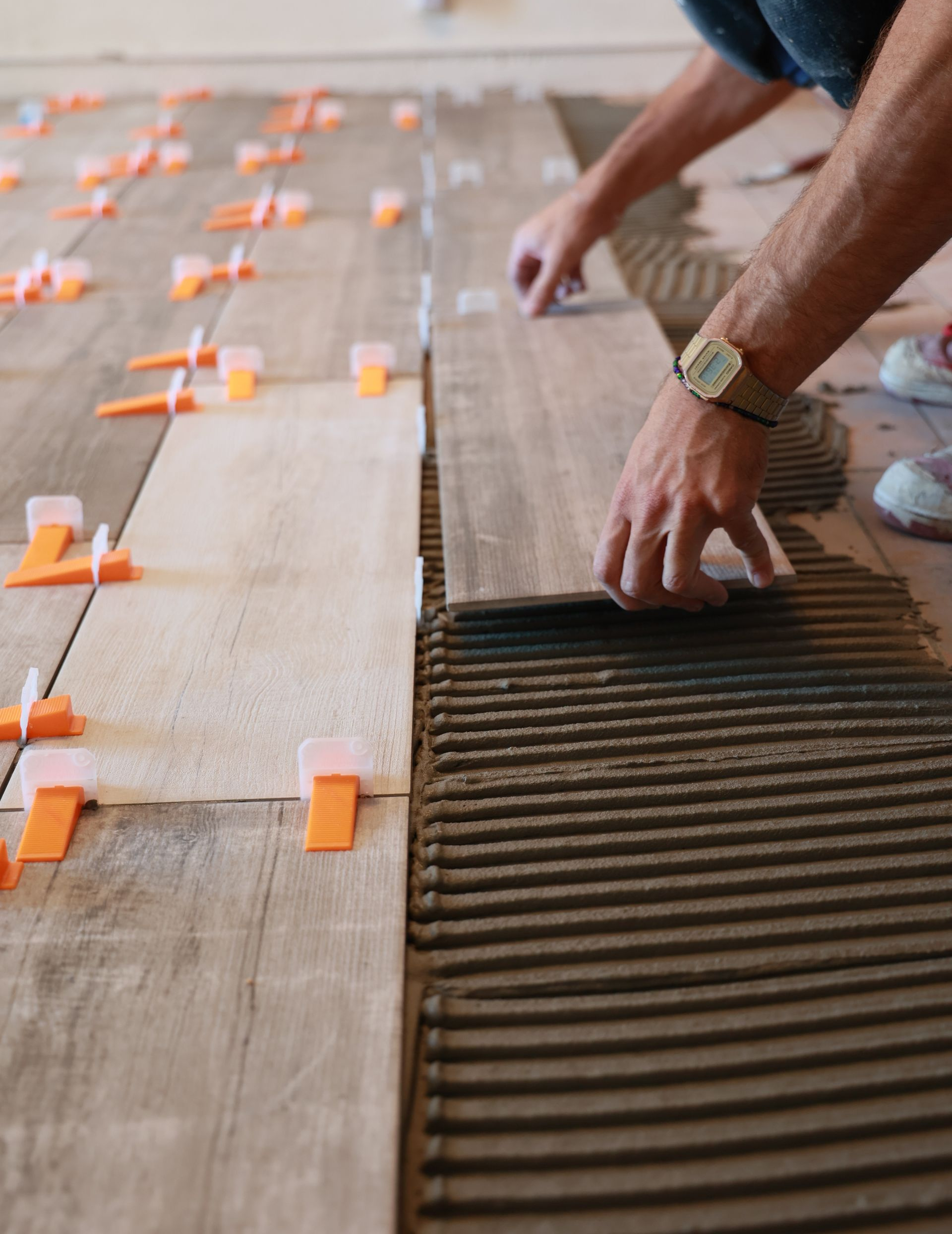 Personne posant du carrelage au sol, appliquant de la colle sur les carreaux et utilisant des clips de nivellement.
