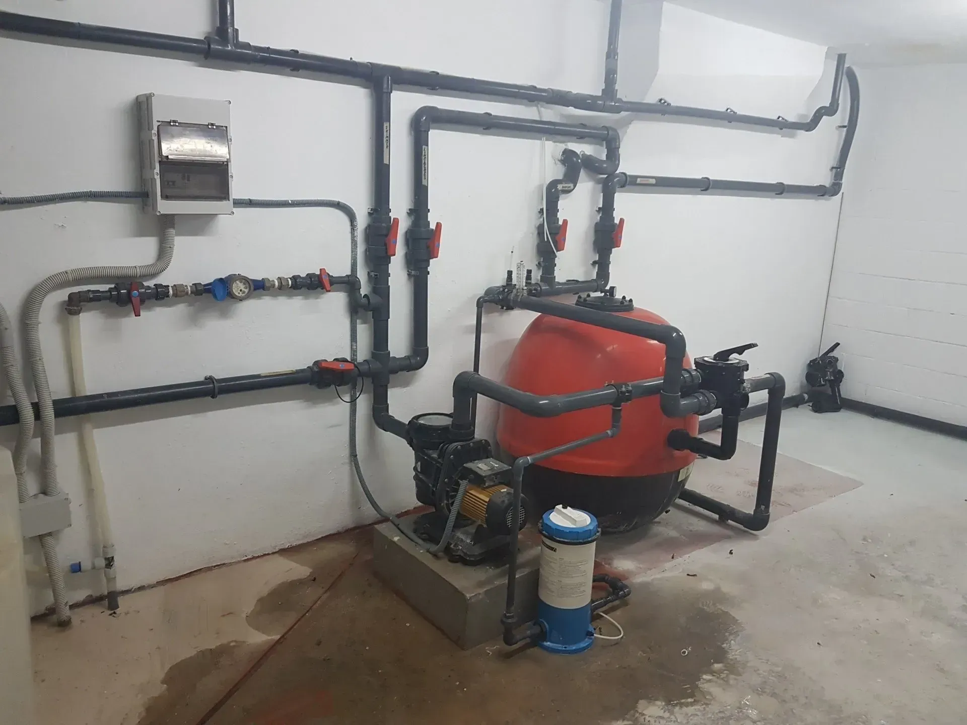 Una habitación con muchas tuberías y un tanque rojo.