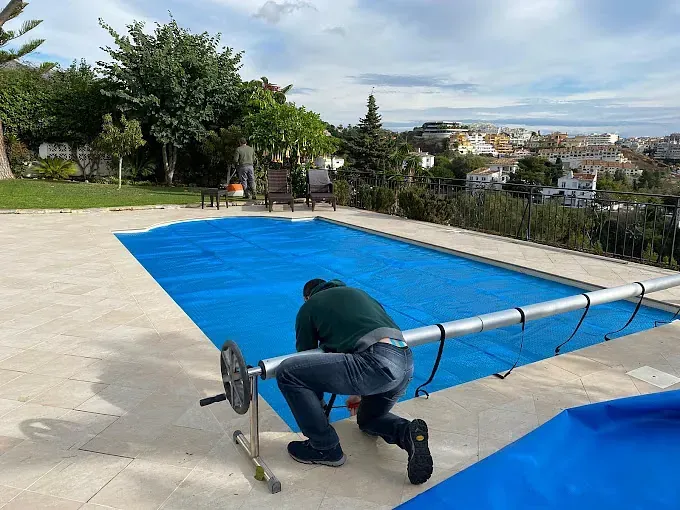 Un hombre está arrodillado junto a una piscina con una cubierta azul.