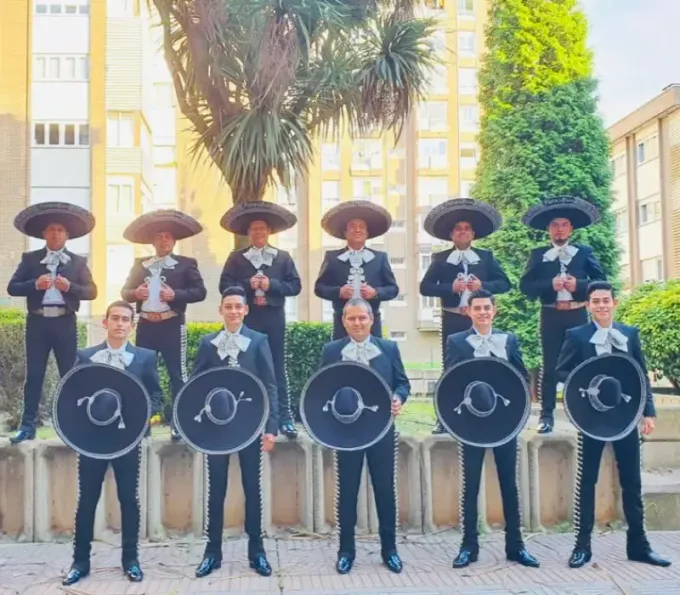 Grupo de mariachis posando al aire libre, vestidos con trajes de charro negros y sombreros, sosteniendo sus instrumentos.