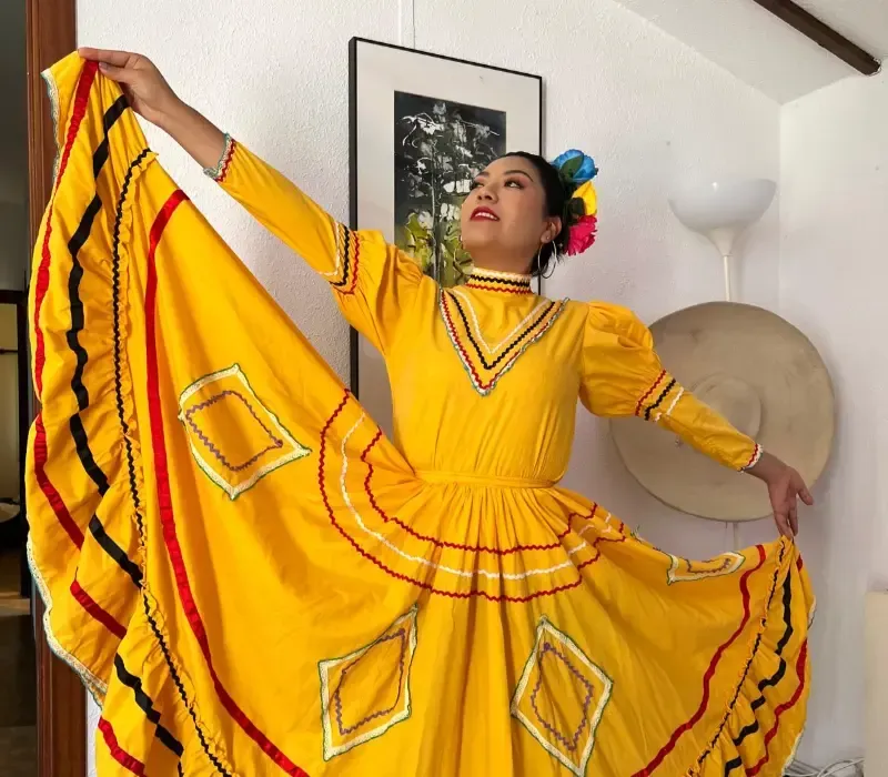 Una mujer vestida con un vestido tradicional mexicano amarillo brillante extiende la falda.
