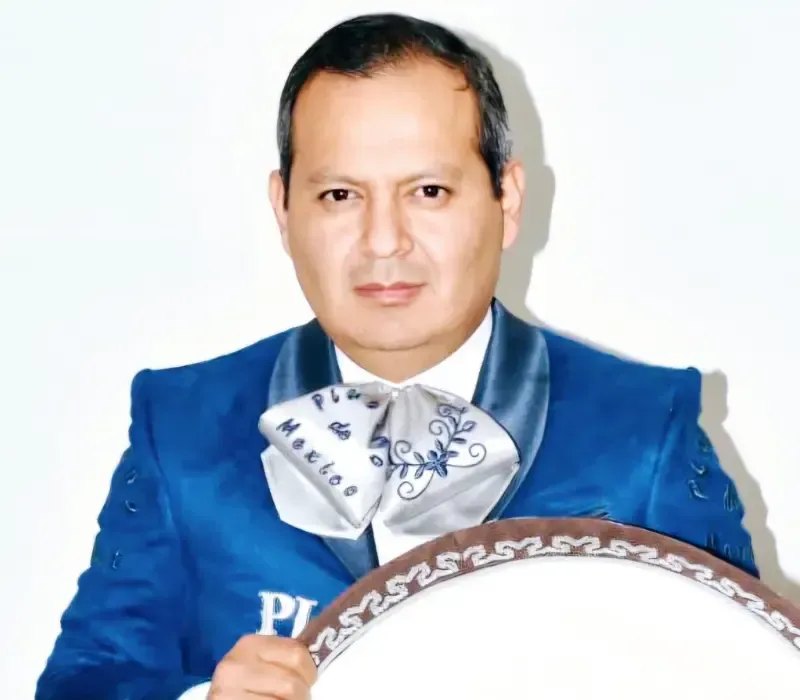 Hombre con traje azul brillante sosteniendo un escudo redondo decorativo sobre un fondo blanco.