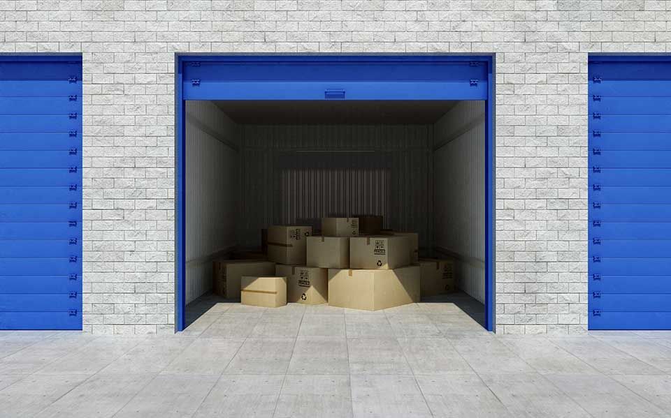 Un box de stockage bleu ouvert contenant plusieurs cartons bruns, adossé à un mur de briques blanches.