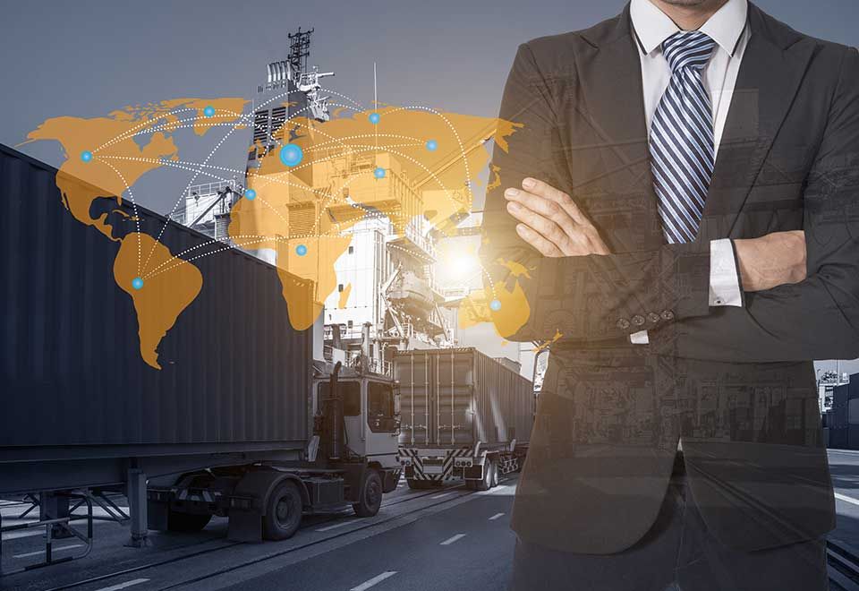 Un professionnel en costume se tient debout, les bras croisés, devant un arrière-plan composé de camions de marchandises et d'une carte du monde numérique.