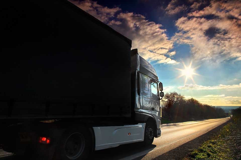 Un camion roule sur une route au coucher du soleil, le soleil brillant de mille feux dans le ciel.