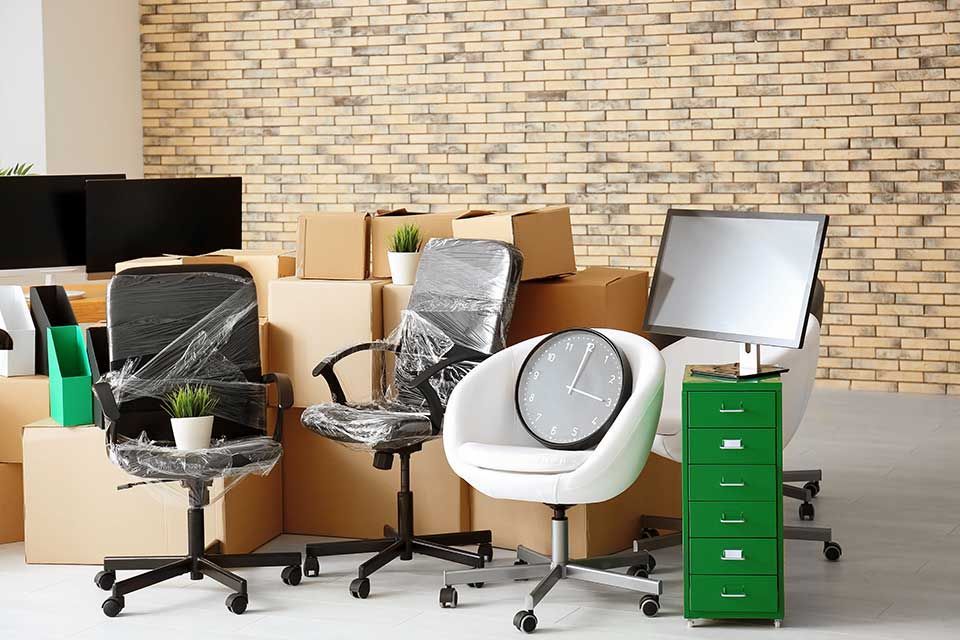 Trois chaises de bureau, un classeur vert avec un écran d'ordinateur et des cartons de déménagement dans un bureau adossés à un mur de briques.