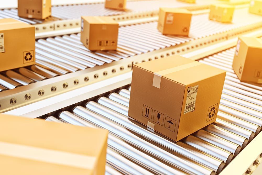 Des colis en carton défilent sur un tapis roulant industriel métallique.