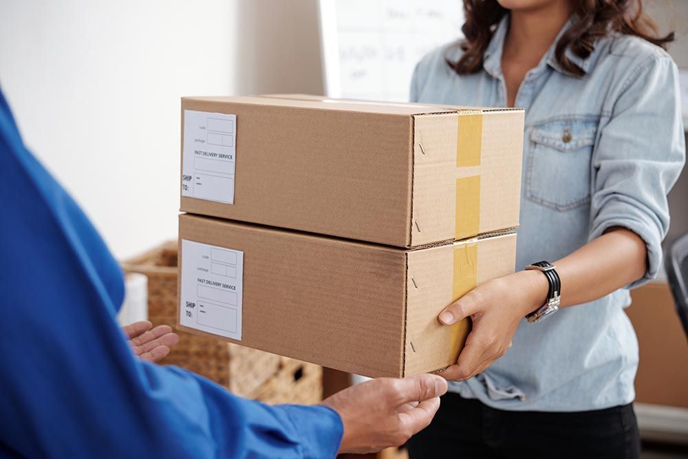 Une personne vêtue d'une chemise bleue tend deux cartons d'expédition empilés à une autre personne portant une chemise en jean bleu clair.