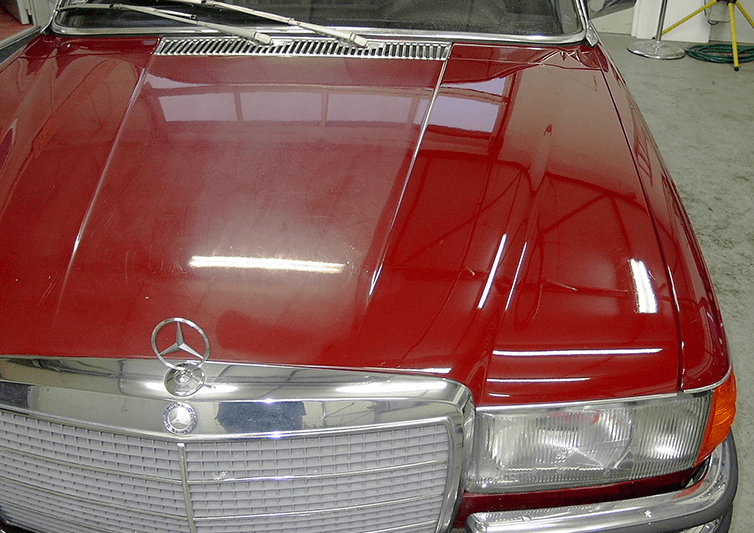 Rote Mercedes-Motorhaube mit Chromgrill und Emblem.