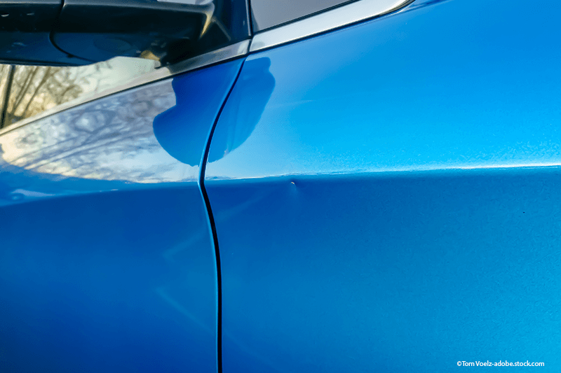Blaue Autotür mit einer Delle.