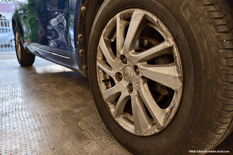 Nahaufnahme eines Autoreifens mit Radkappe. Die Felge ist silberfarben und etwas verschmutzt; das Auto ist blau.