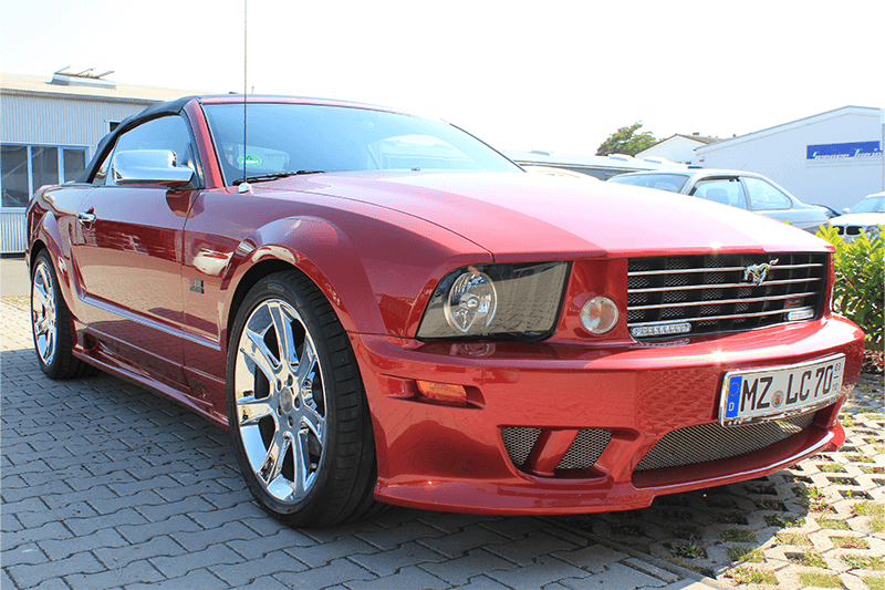 Ein rotes Ford Mustang Cabriolet mit Chromfelgen steht im Freien.