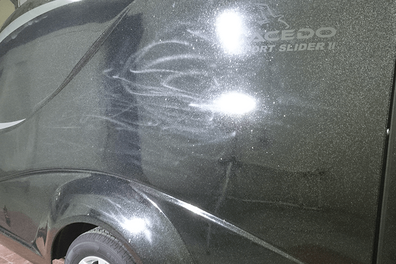 Dunkle Fahrzeugseite mit Kratzern, einem Rad und dem Schriftzug „SAGE DO SPORT SLIDER II“.