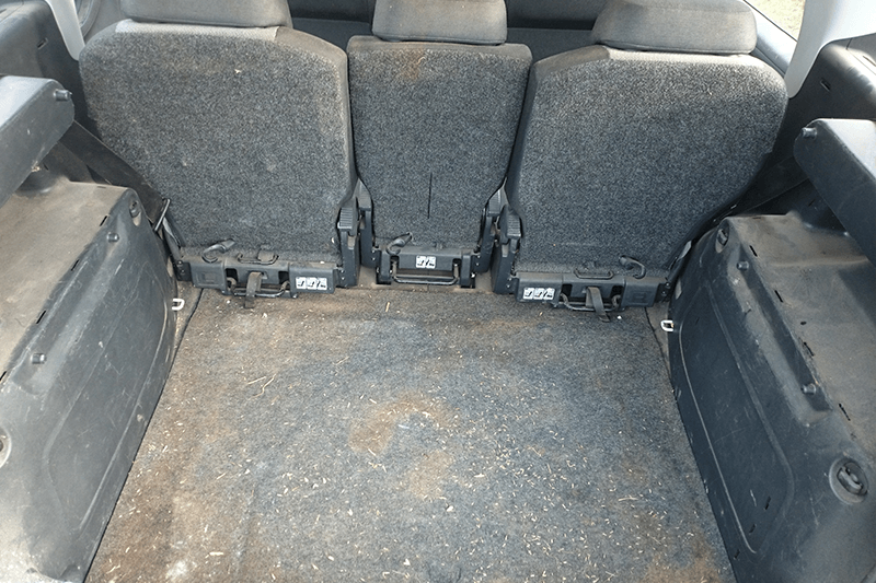 Rücksitz eines Fahrzeugs mit drei aufrechten Sitzen; dunkle Polsterung und schmutziger Boden.