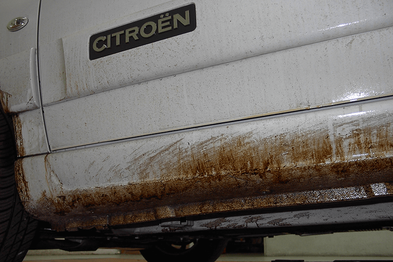 Mit Schlamm bespritzte weiße Citroën-Autotür und Schwellerverkleidung, auf der das Citroën-Logo noch sichtbar ist.