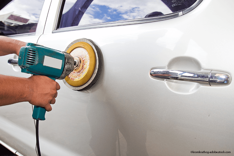 Eine Person poliert die Seite eines weißen Autos mit einer Poliermaschine.
