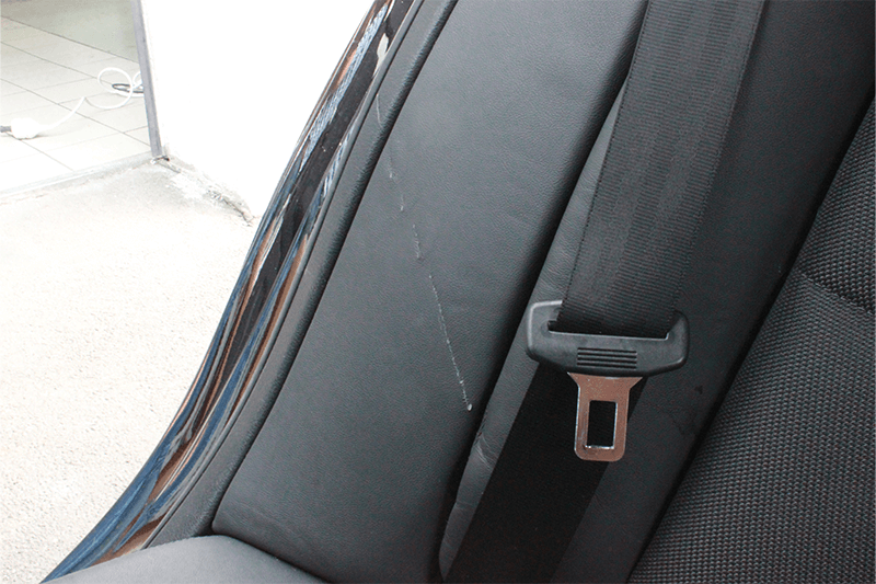 Schwarzer Autositz mit Sicherheitsgurt, der Kratzer im Leder aufweist.