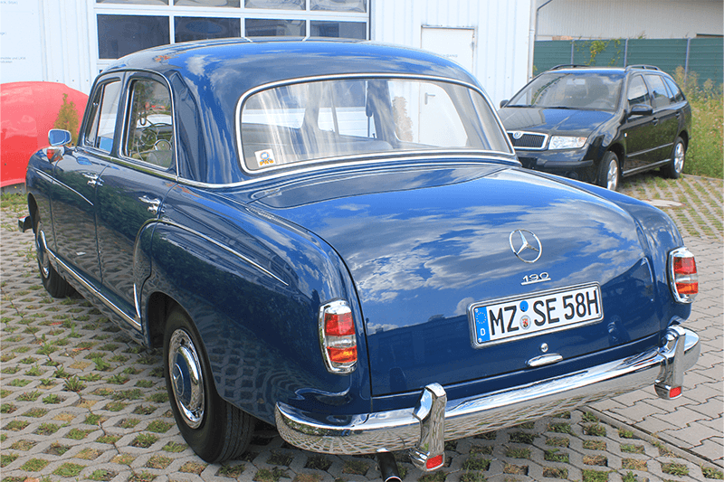 Eine blaue Mercedes-Benz Oldtimer-Limousine parkt im Freien; im Hintergrund ist ein schwarzes Auto zu sehen.
