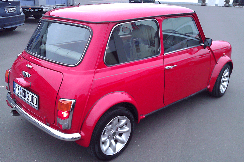 Ein roter Mini Cooper Oldtimer parkt auf einem gepflasterten Parkplatz.