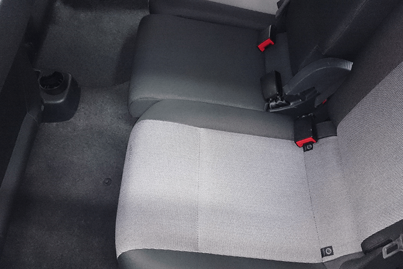 Graue und schwarze Rückbank eines Autos mit Sicherheitsgurten vor grauem Teppichboden.