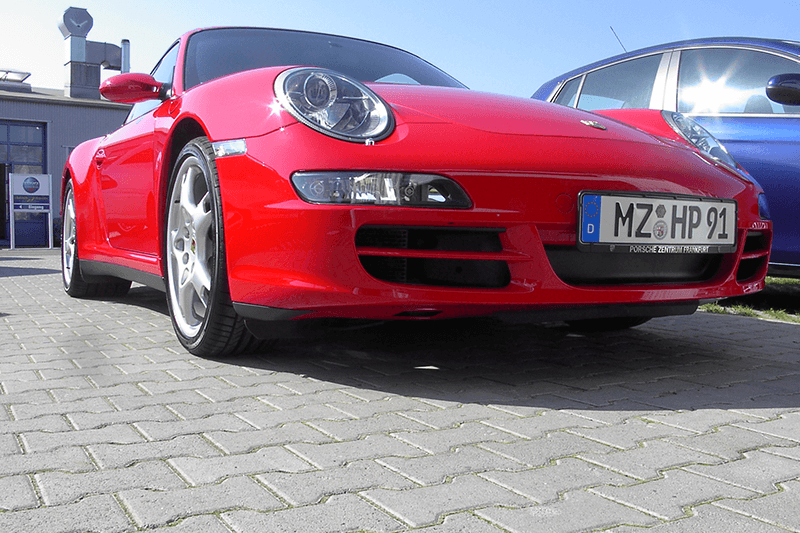 Ein roter Porsche-Sportwagen parkt auf Kopfsteinpflaster.