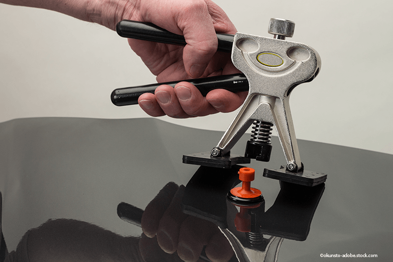 Eine Hand benutzt einen Ausbeulhebel, um die schwarze Oberfläche eines Autos zu reparieren.