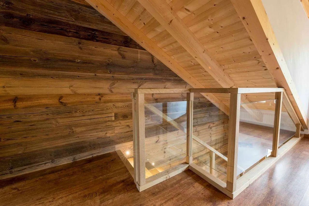 Combles aménagés en bois avec poutres apparentes et barrière de sécurité à panneaux transparents.