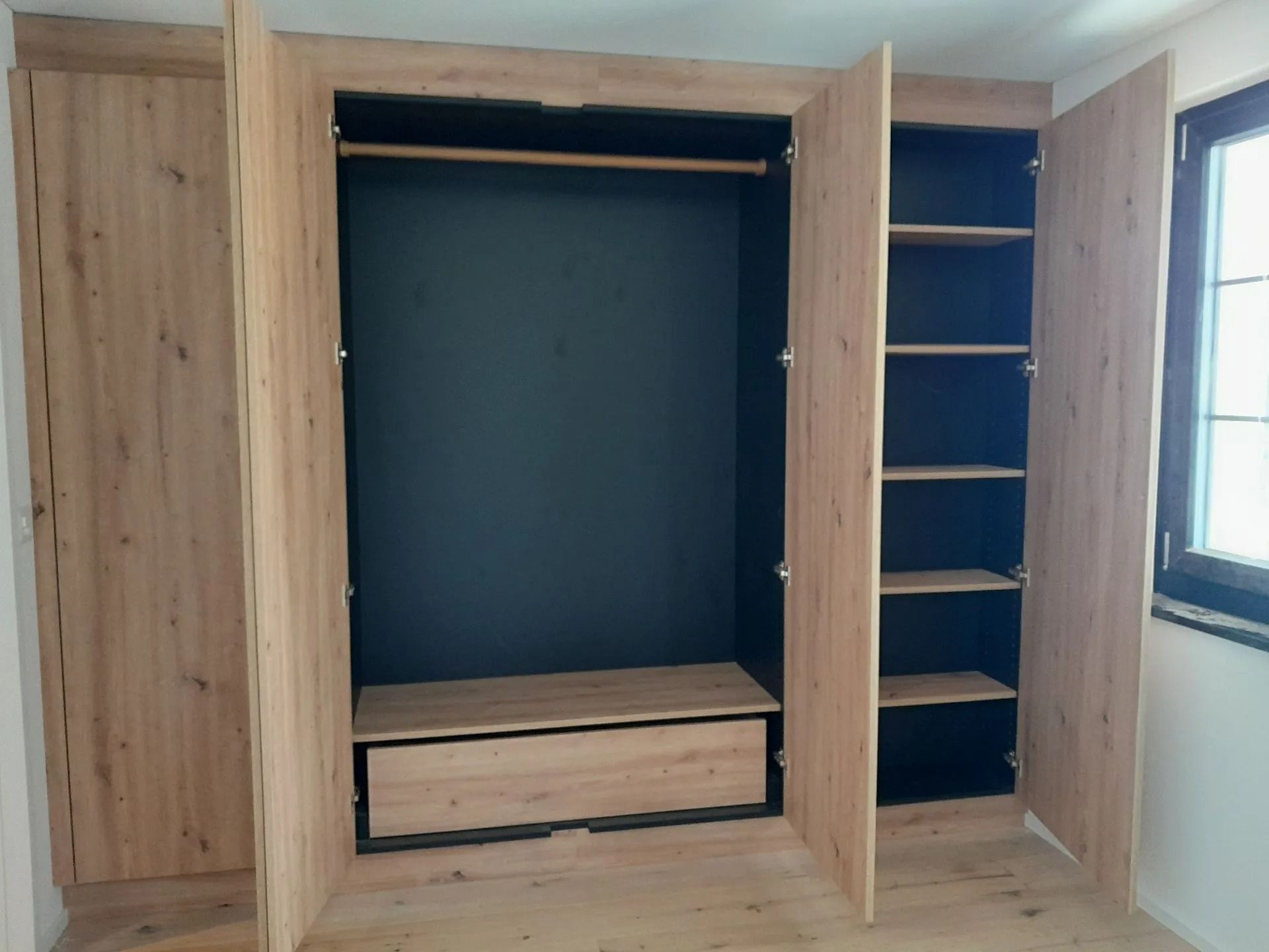 Armoire en bois à portes ouvertes, comprenant une tringle à vêtements, des étagères et un tiroir.