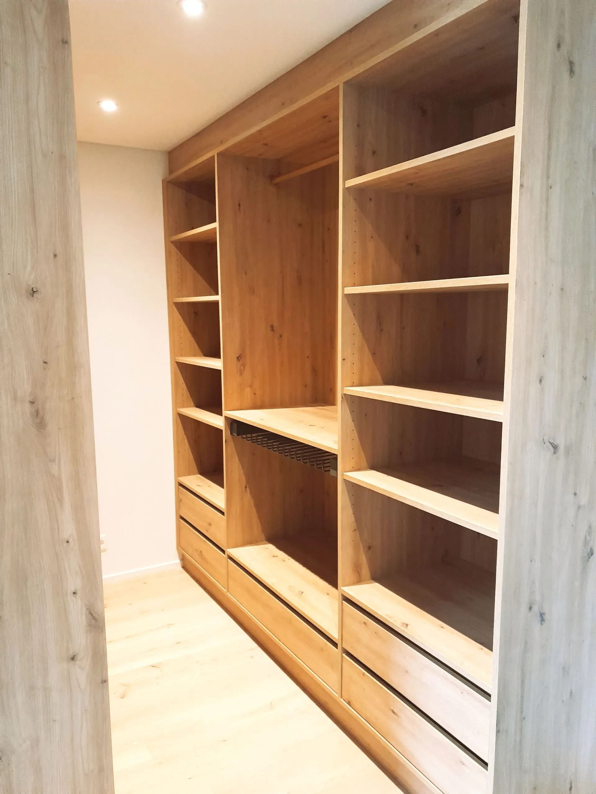 Armoire en bois avec étagères, tiroirs et tringle à vêtements, encastrée dans un mur.