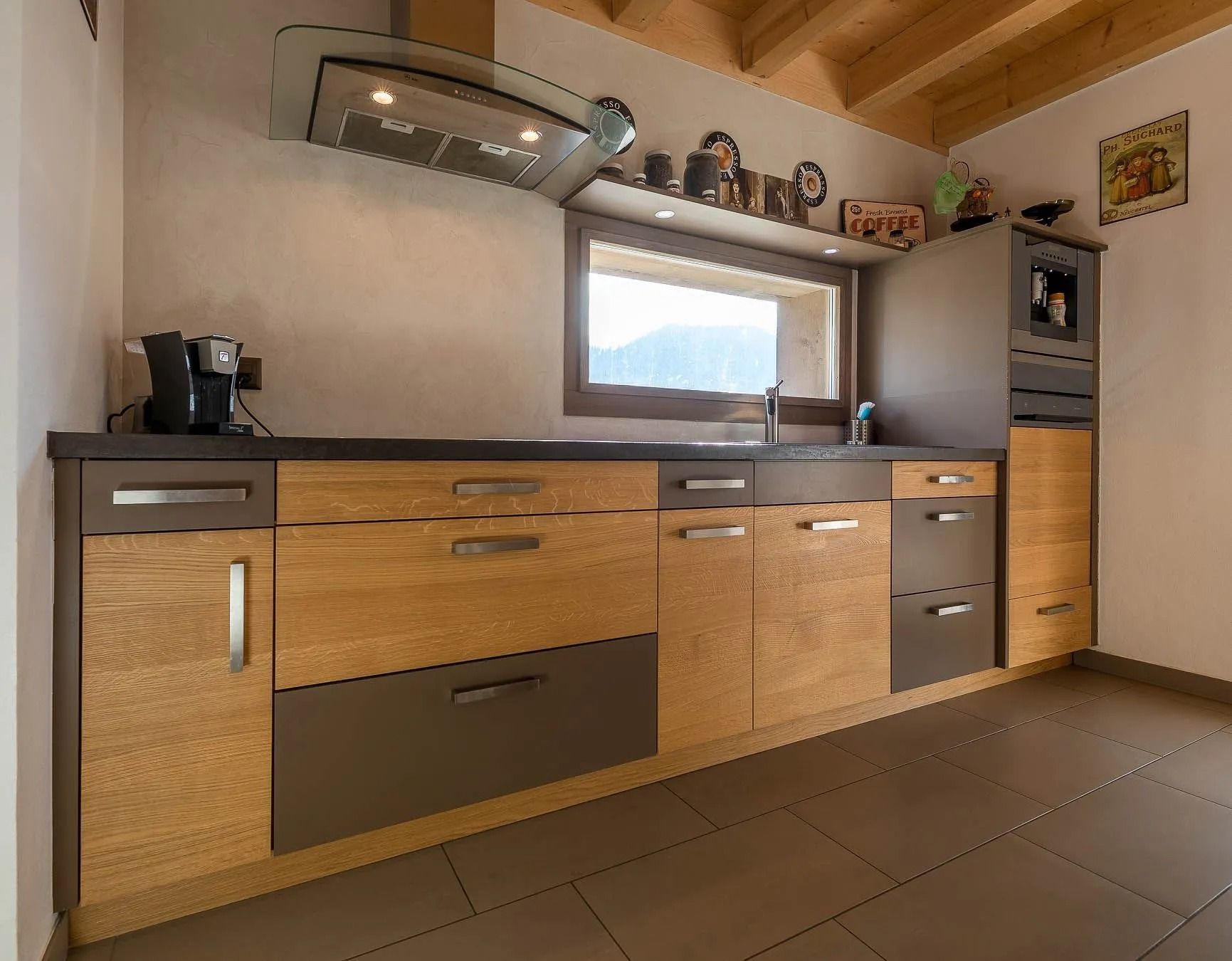 Cuisine avec armoires en bois et comptoirs foncés, sous une fenêtre.