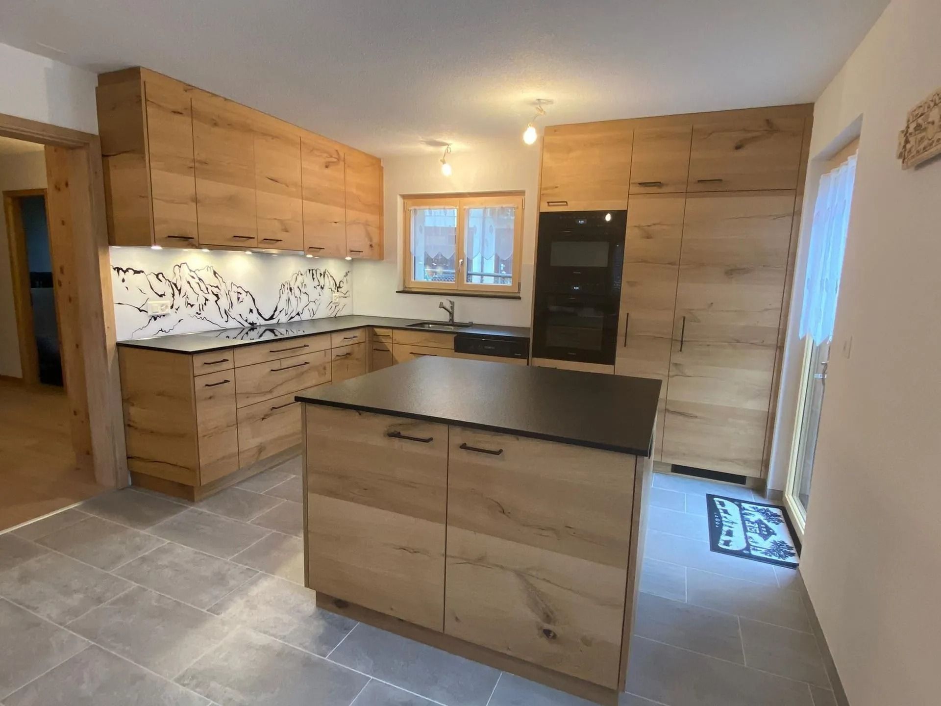 Cuisine moderne avec armoires et îlot en bois, comptoirs gris et sol carrelé.