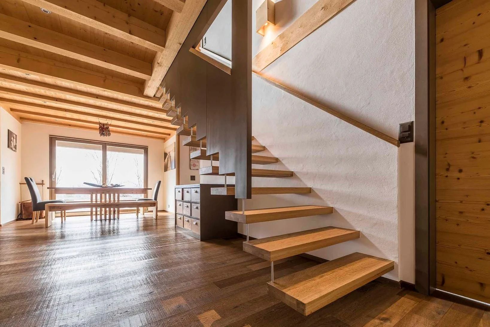 Escalier en bois avec poutres apparentes, menant à l'étage. Intérieur lumineux et moderne.