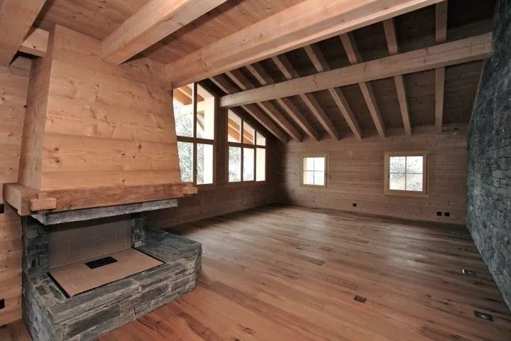 Intérieur en bois avec cheminée en pierre, fenêtres et poutres apparentes.