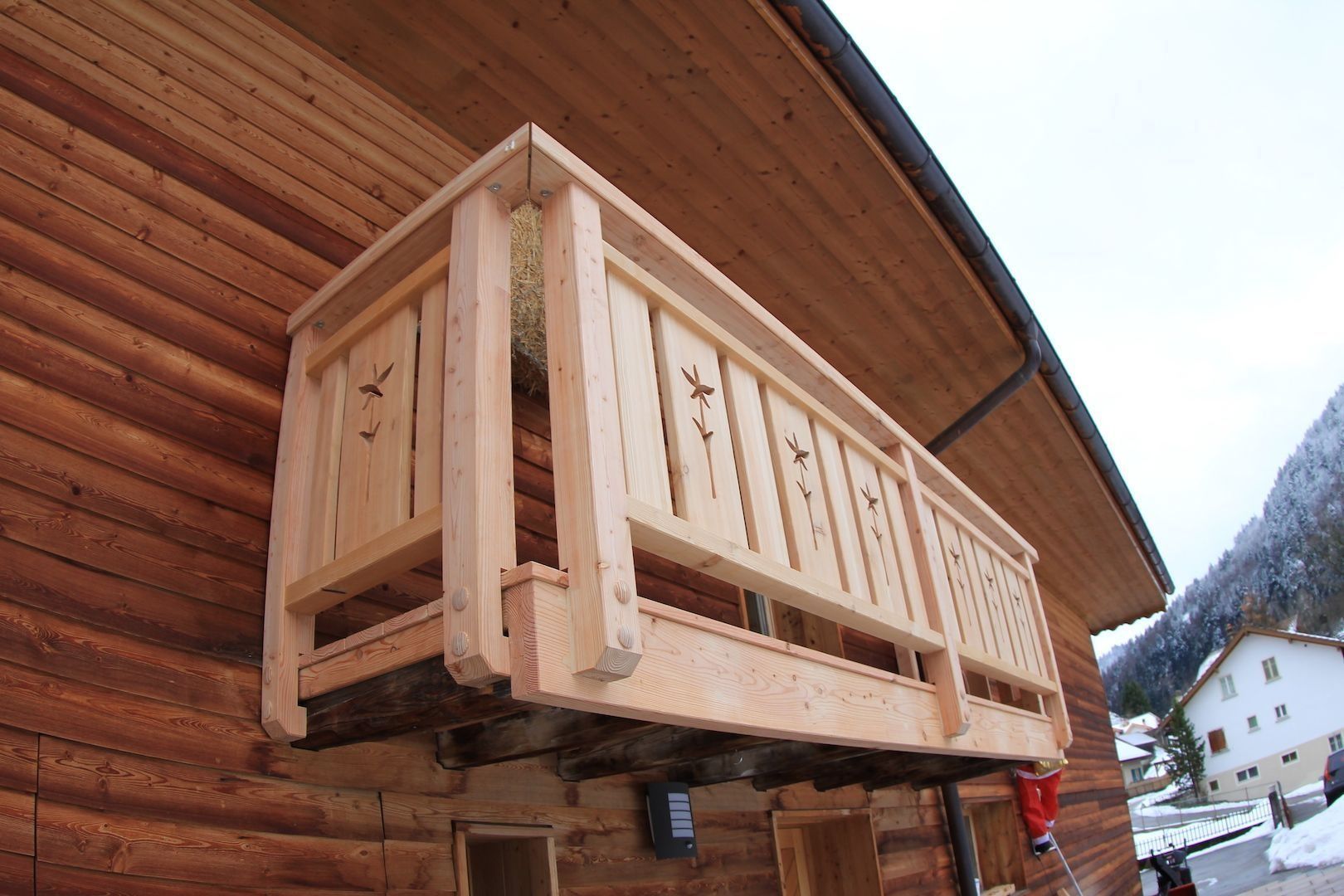 Balcon en bois orné de détails sculptés sur le côté d'une cabane en rondins bruns.