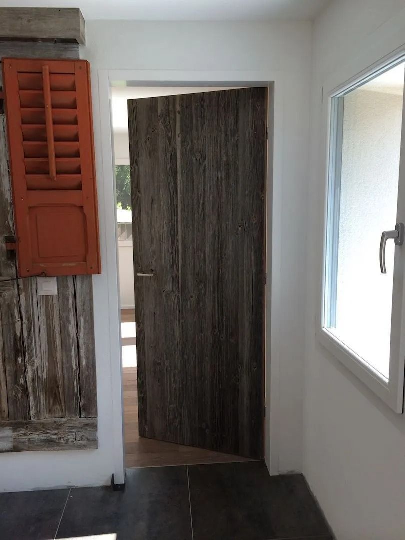 Porte d'entrée avec porte en bois patiné, volet orange et fenêtre.