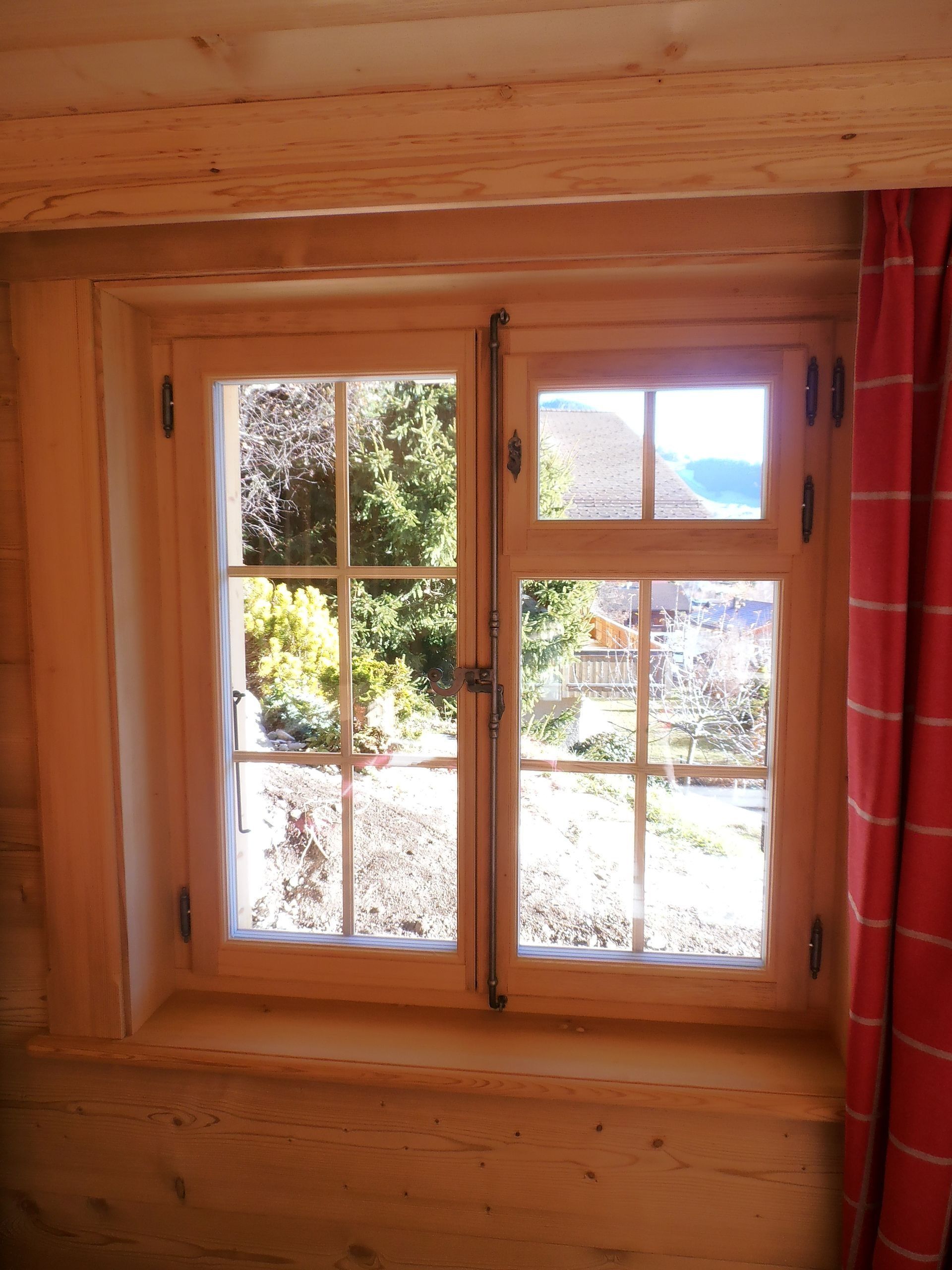 Fenêtre en bois donnant sur un jardin et les montagnes ; rideau rouge à droite.