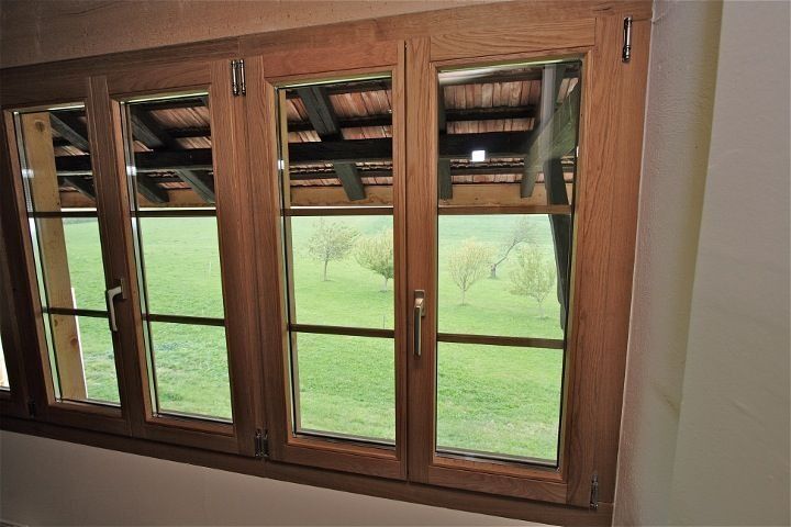 Fenêtres à châssis en bois donnant sur un champ verdoyant. Châssis bruns et vitres transparentes.