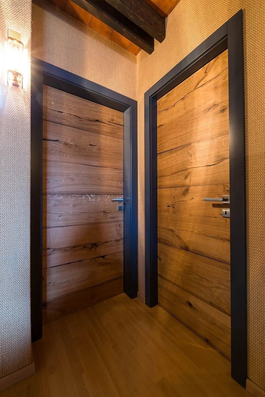 Deux portes en bois à encadrement foncé dans un couloir, parquet et murs texturés.