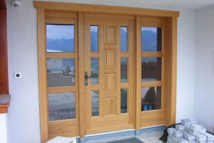 Porte d'entrée en bois avec panneaux de verre et imposte latérale dans un cadre clair.