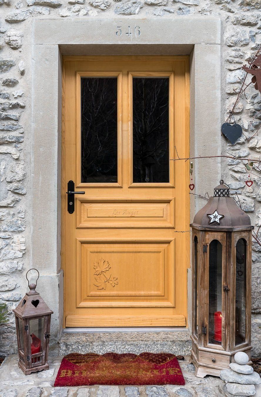 Porte en bois avec imposte dans un cadre en pierre ; lanternes et paillasson.