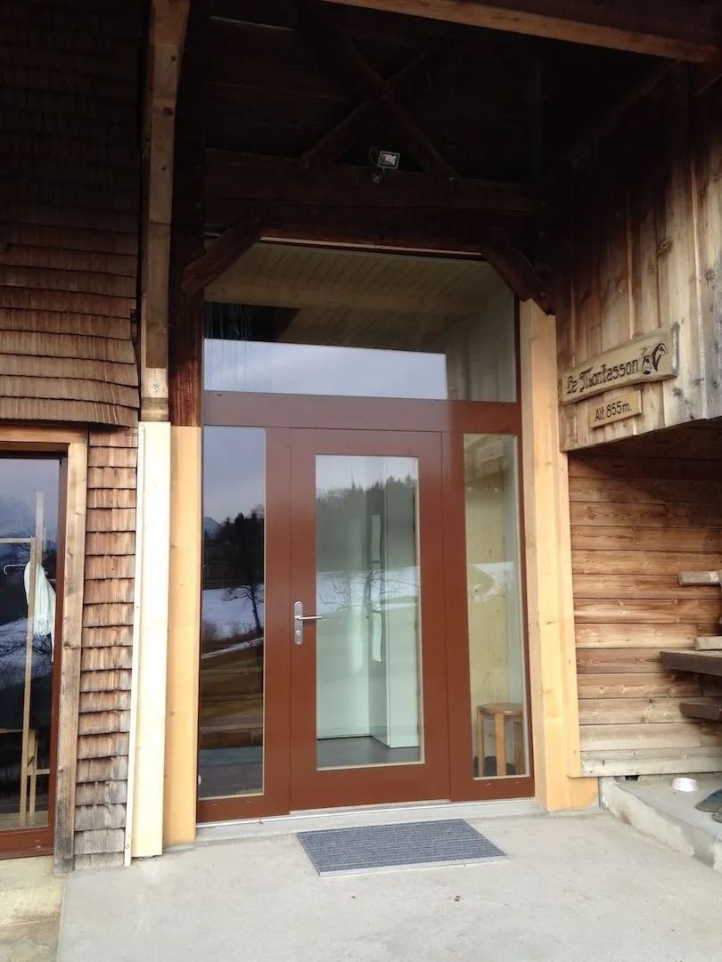 Porte d'entrée en bois brun avec panneaux de verre sur un bâtiment en bois.