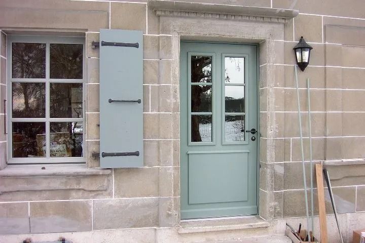 Porte, une fenêtre et des volets bleu clair. Une lanterne est fixée à côté de la porte.