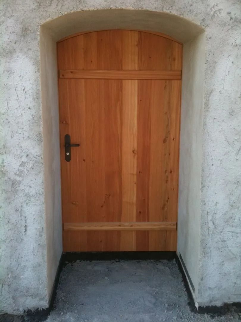 Porte en bois avec poignée noire encastrée dans une embrasure de porte cintrée blanche.