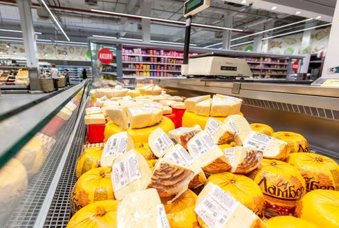 Una vitrina en una tienda de comestibles llena de diversas ruedas y cuñas de queso amarillo.
