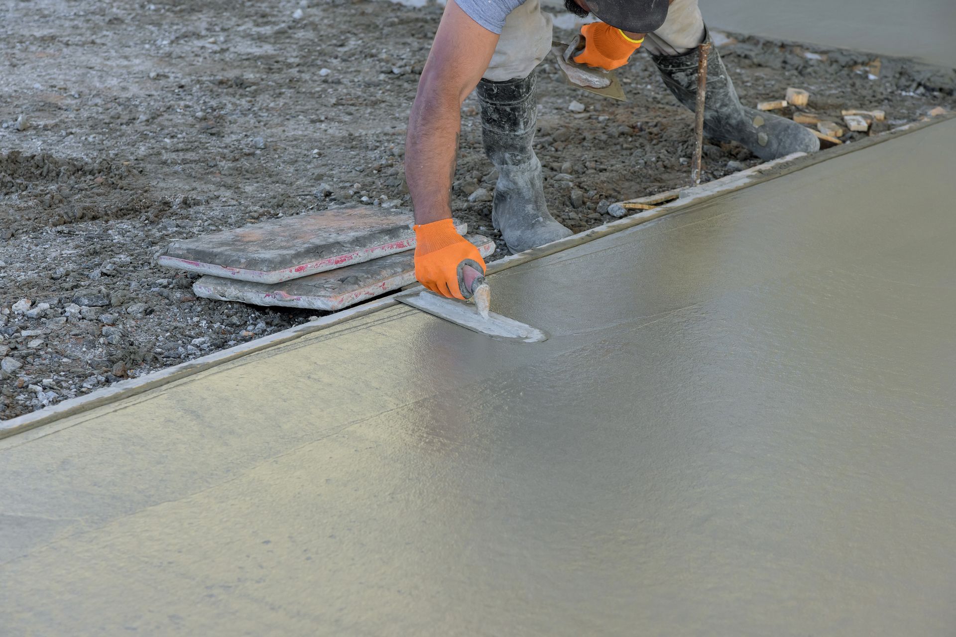 Un ouvrier lisse du béton frais à la truelle sur un chantier de construction.