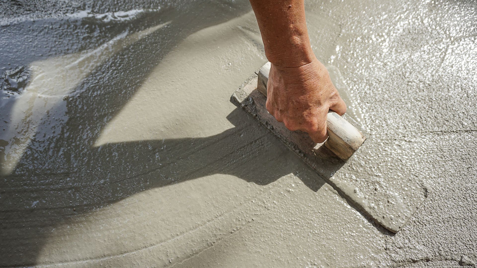 Lissage manuel du béton humide à la truelle sur une surface ensoleillée