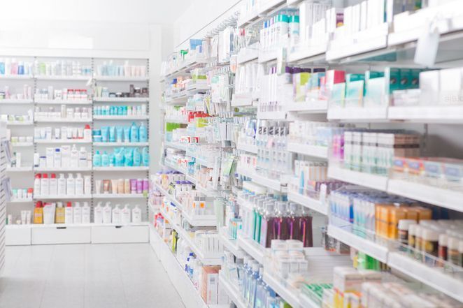 Pasillo de farmacia luminoso con estantes de medicamentos y artículos de tocador variados a ambos lados.