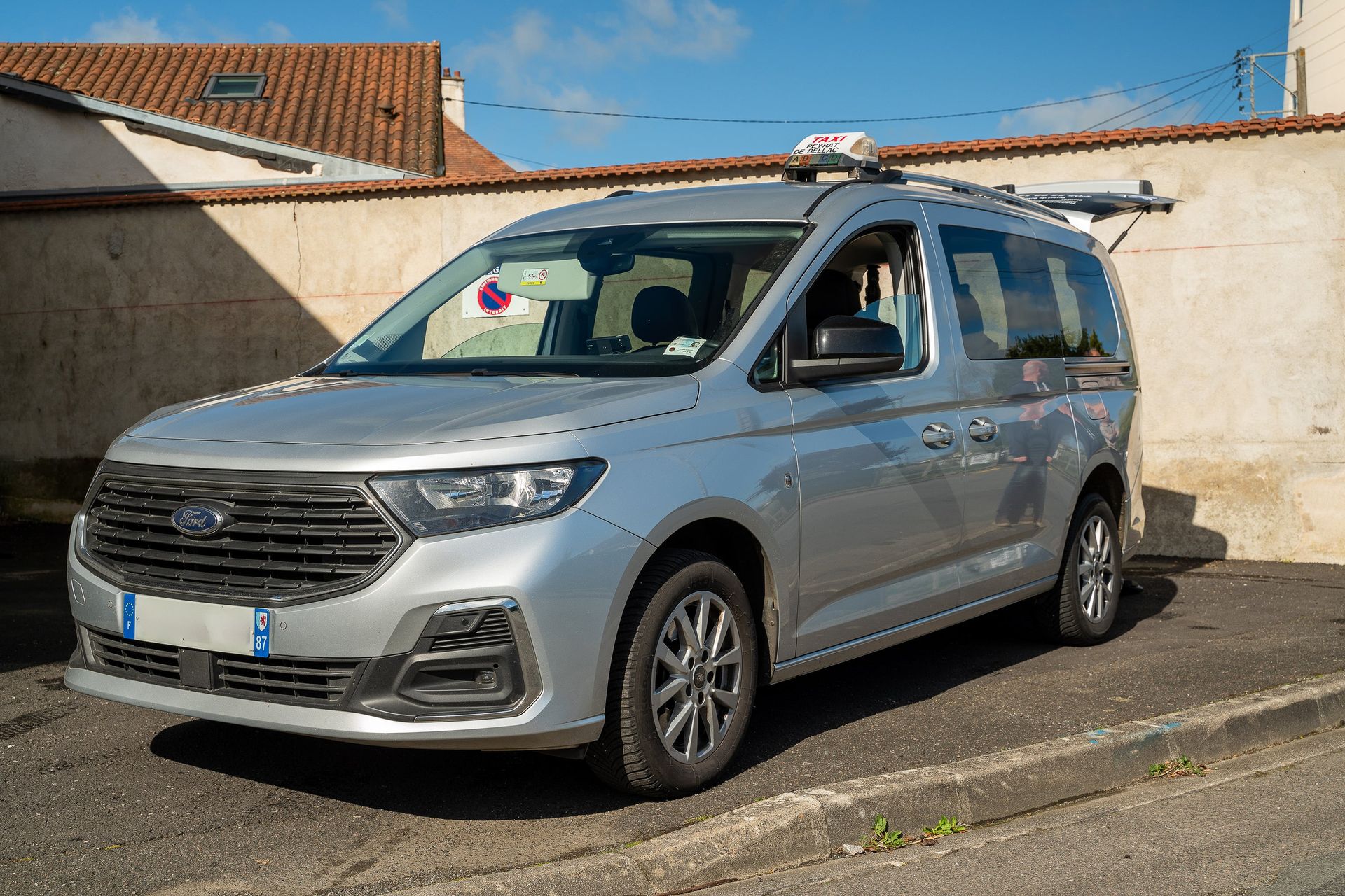 Un taxi argenté stationné près d'un bâtiment par une journée ensoleillée.